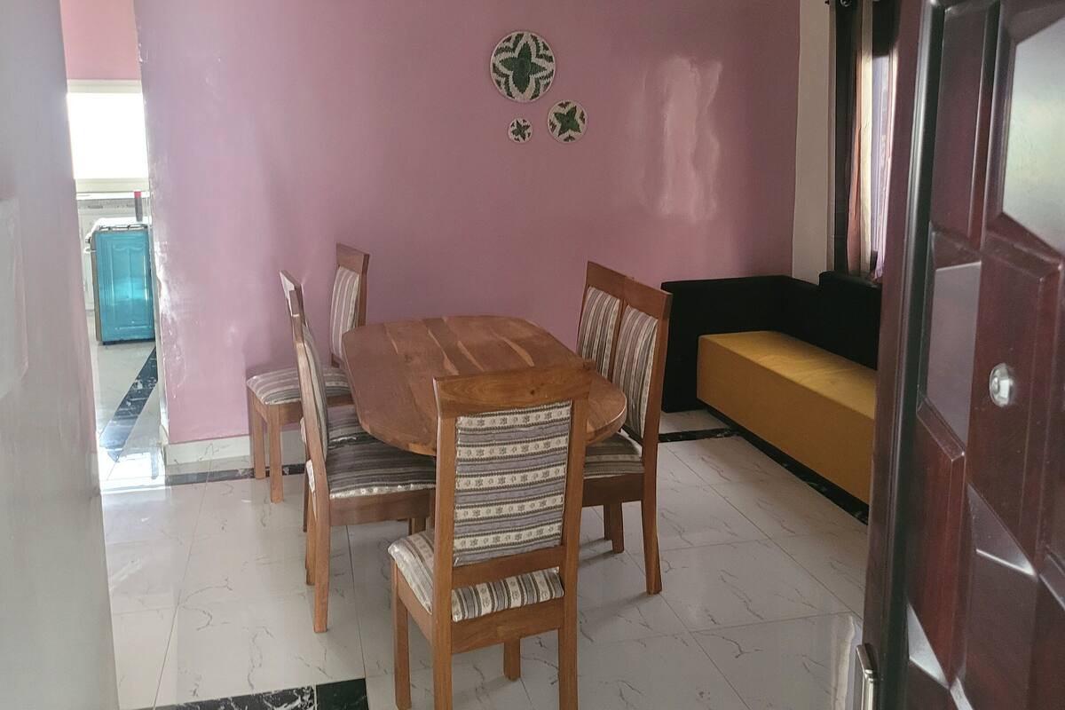 A dining area with a wooden table and chairs, a pink wall, and a small round mirror.