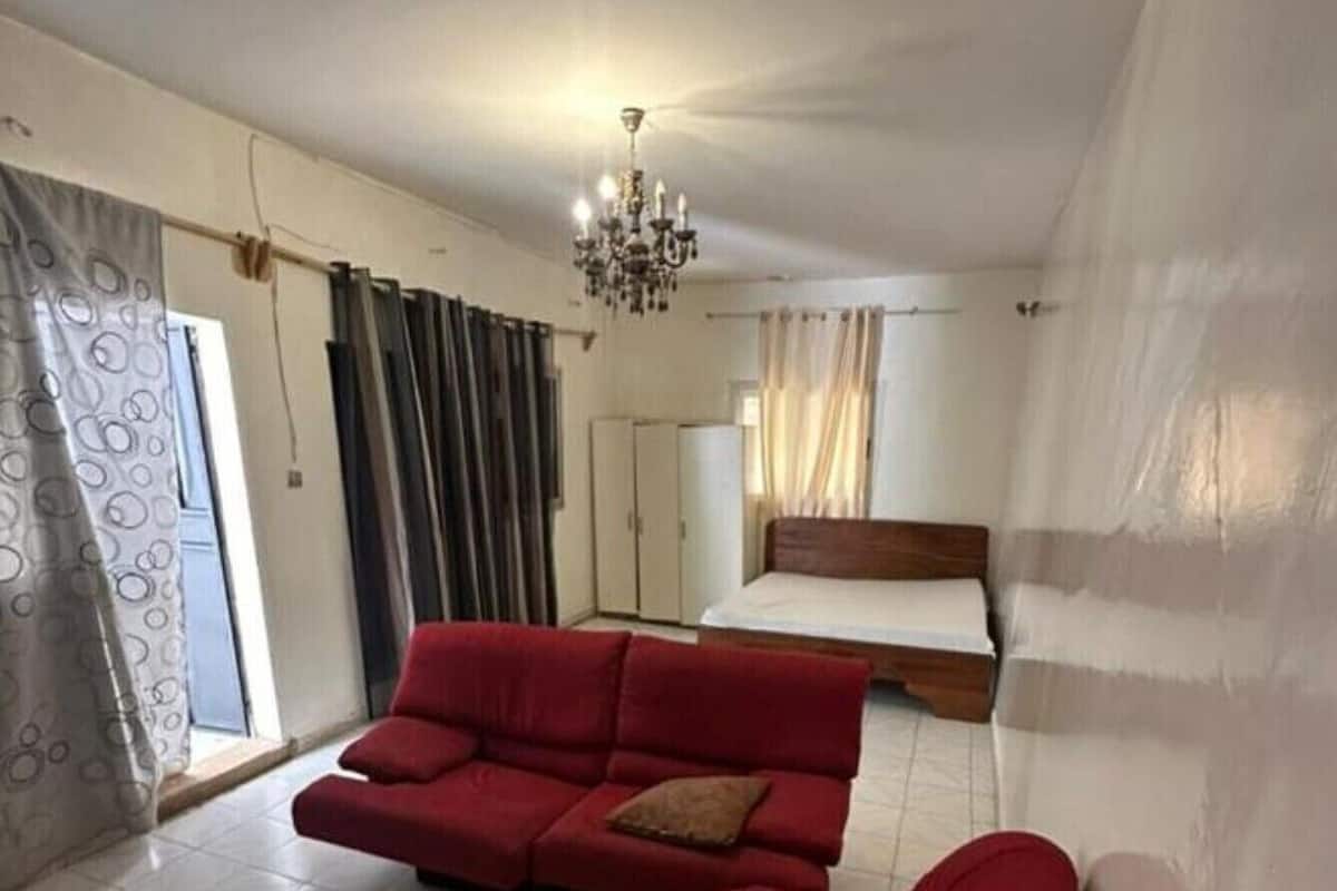 A room with a large bed, a red sofa, a chandelier, and a wardrobe.
