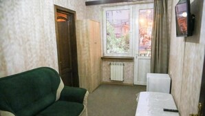 Una habitación pequeña con un sofá verde, una mesita con mantel blanco, un radiador y una ventana con cortinas.