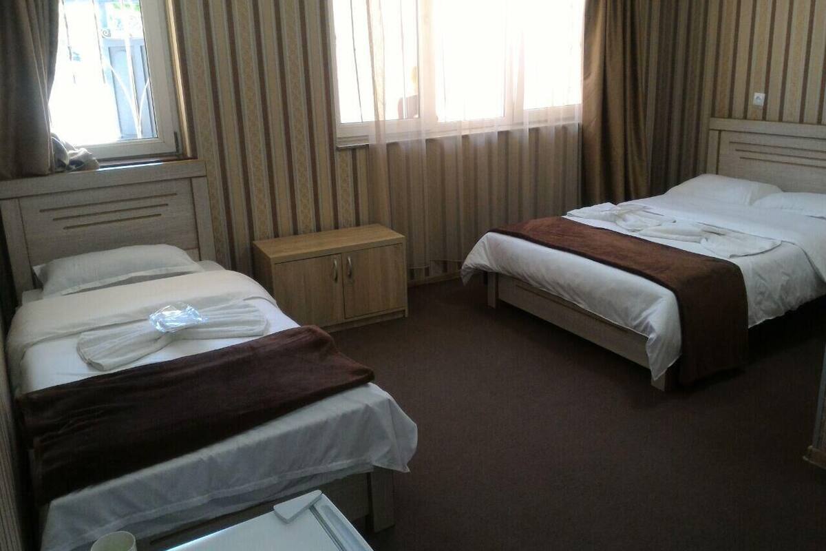 A hotel room with two single beds, a wooden cabinet, and a window with curtains.