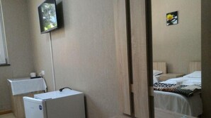 Habitación de hotel con cama, un refrigerador pequeño, cómoda de madera, espejo y televisor montado en la pared.