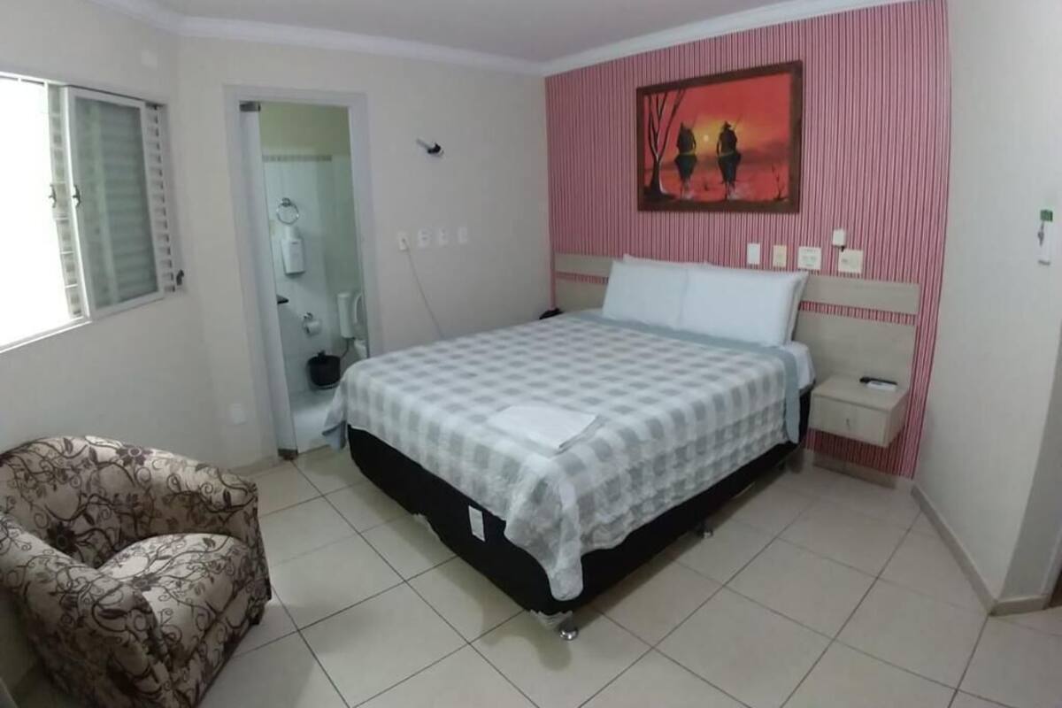 A bedroom with a bed, a chair, a painting on the wall, and a window.
