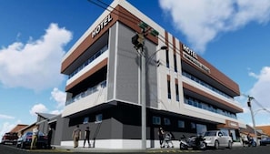 Un hotel de varios pisos con un llamativo letrero 'HOTEL' en la fachada, techo plano y un estacionamiento al frente.