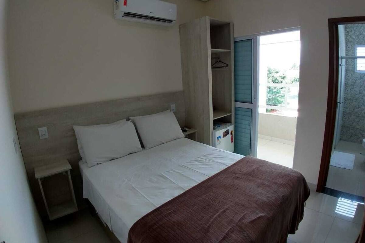 A bedroom with a bed, a nightstand, an open closet, and a sliding glass door to the outside.