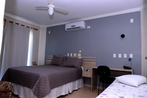 Un dormitorio con cama, escritorio, silla, aire acondicionado y ventana con cortinas.