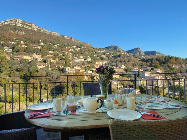 A dining table set outdoors with a view of a mountainous town.