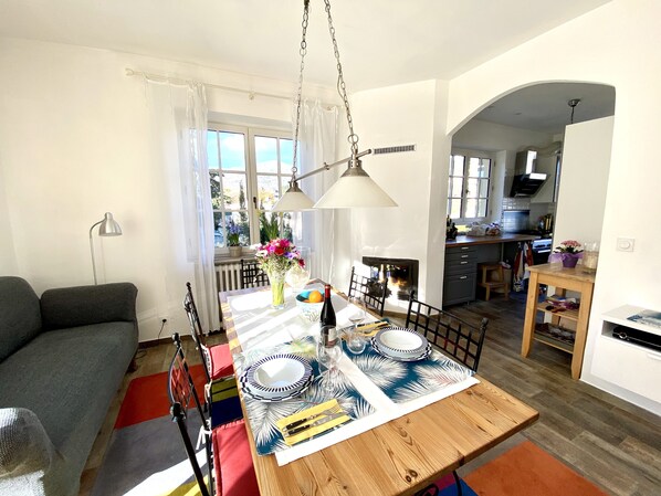 Een eetgedeelte met een houten tafel voor vier personen, een bank en een keuken op de achtergrond.