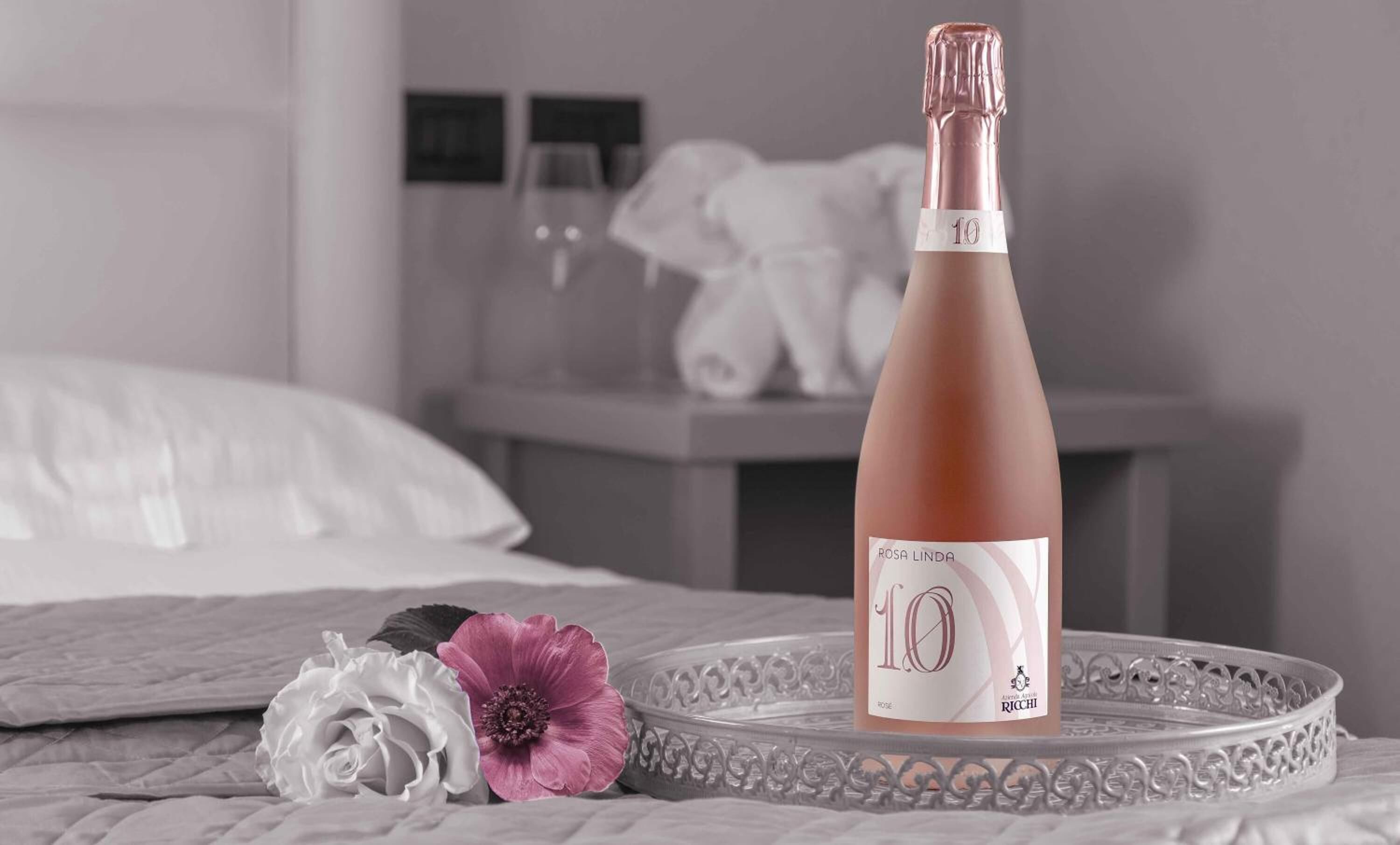 Una botella de vino Rosa Linda 10 sobre una bandeja con una rosa blanca y una flor rosa.