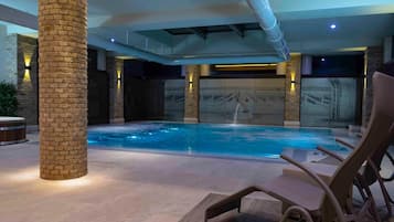 Una piscina interior con agua cristalina, rodeada de sillones de descanso y un pilar de piedra.