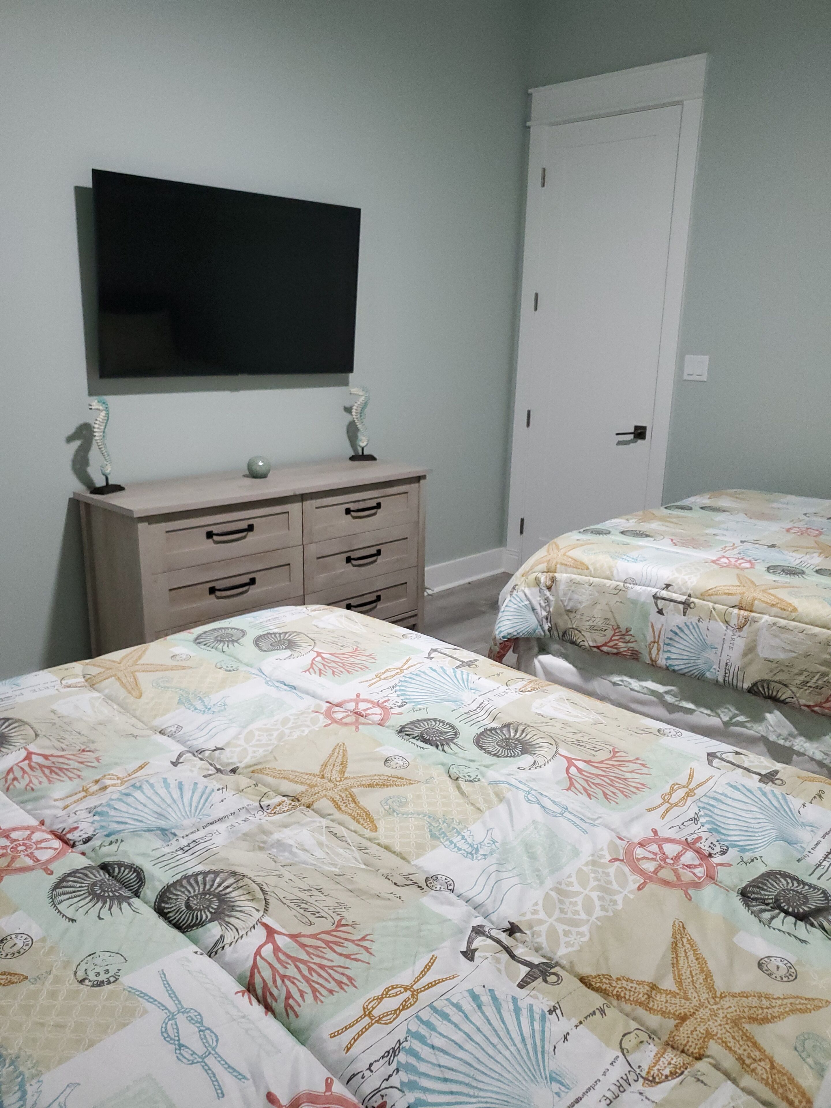 Un dormitorio con dos camas, un aparador, un televisor y una puerta.