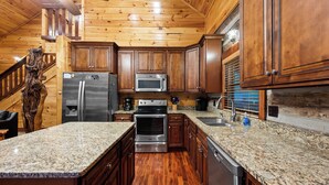 Una cocina con armarios de madera, encimeras de granito, electrodomésticos de acero inoxidable y una escalera de madera.
