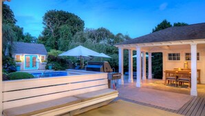 Un giardino con piscina, zona barbecue e patio coperto con mobili da esterno.