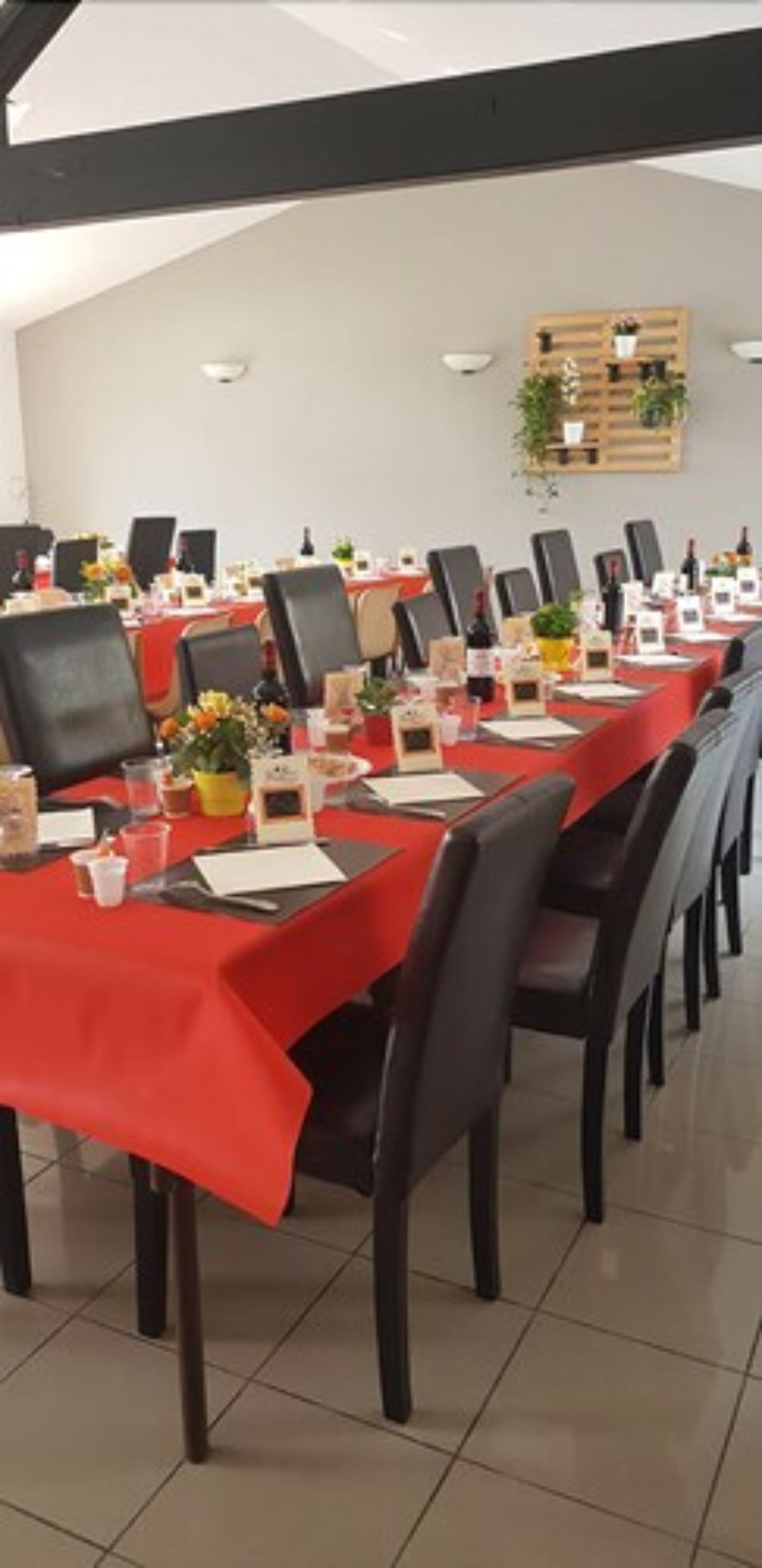 Une salle de conférence avec de longues tables recouvertes de nappes rouges, équipée de chaises, de porte-noms et de divers objets, comme des bouteilles et de petites plantes en pot.