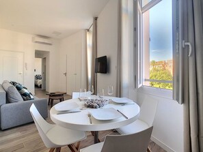 A modern dining area with a round table, white chairs, and a view of greenery outside.
