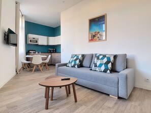 A modern living room with a grey sofa, a coffee table, and a kitchen in the background.