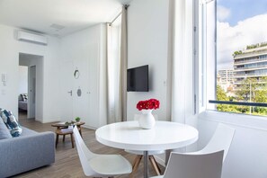 A modern living room with a round white table, a grey sofa, and a TV mounted on the wall.