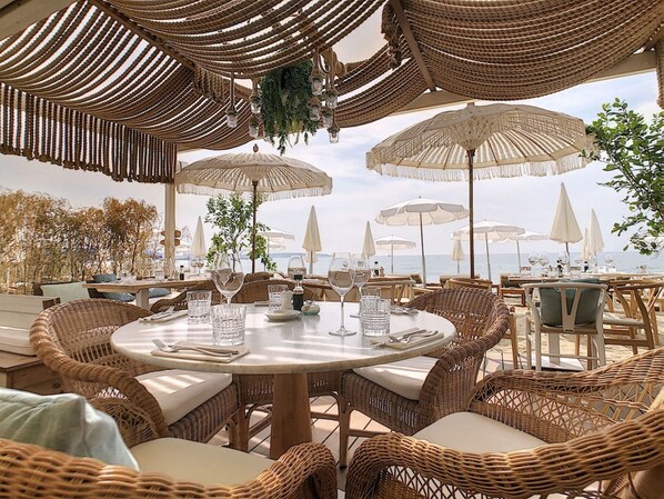 An outdoor dining area with wicker furniture, round tables, and white umbrellas.