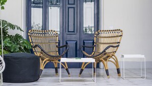Deux chaises en osier, avec une table blanche devant une porte bleu foncé.