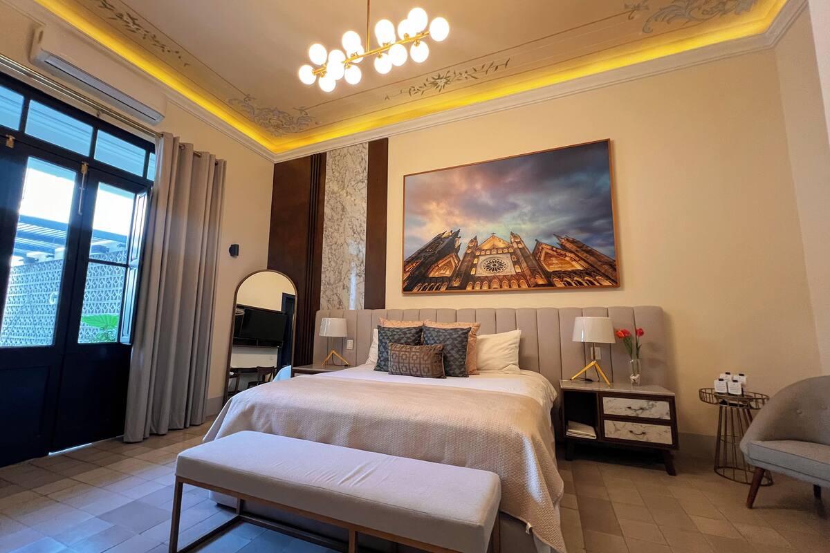 A hotel room with a large bed, a bench, a desk, and a chair.