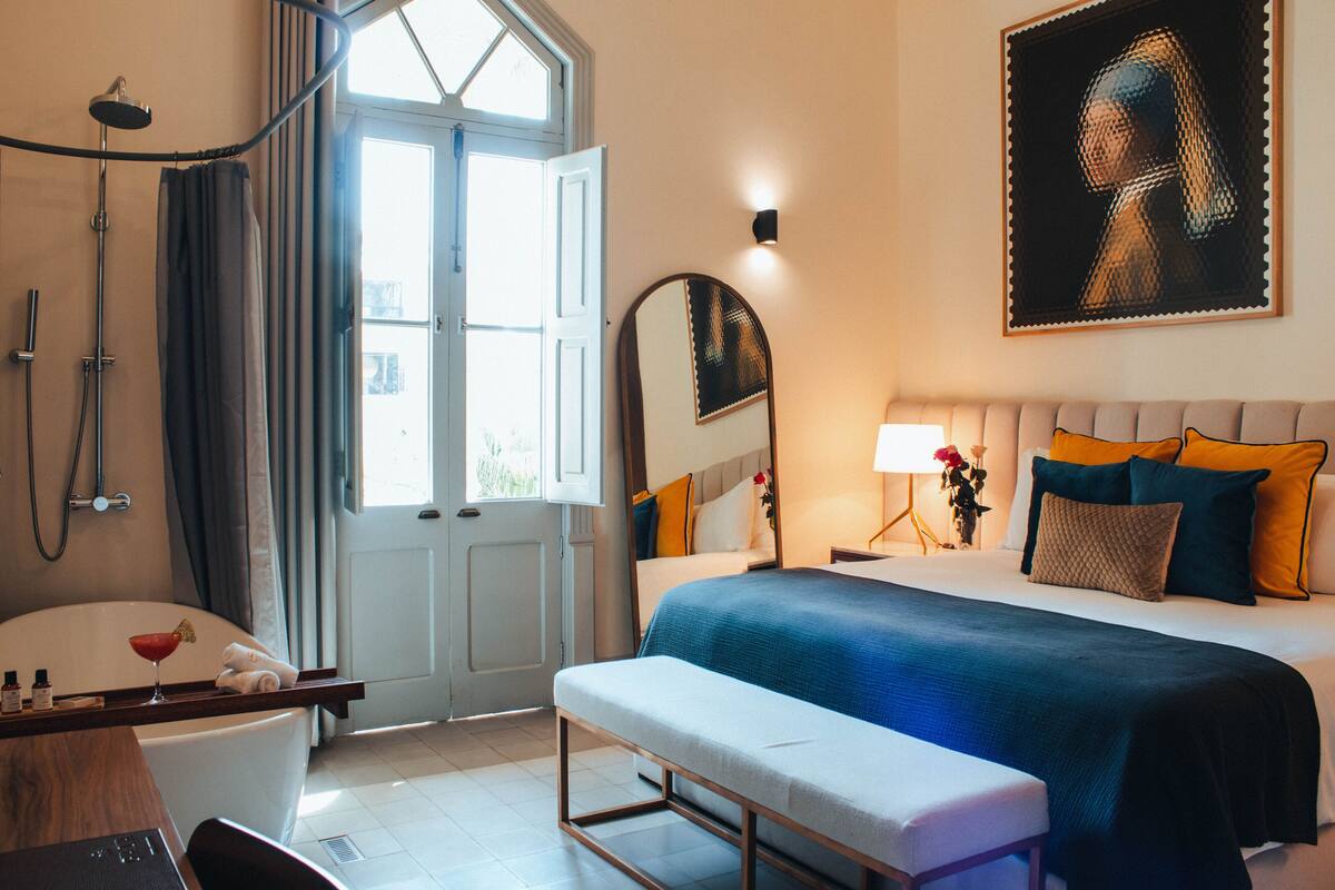 A hotel room with a large bed, a bench, a bathtub, and a shower.
