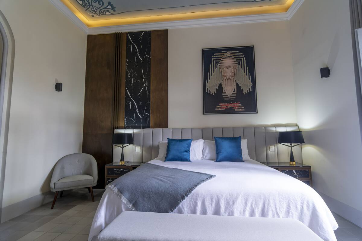 A hotel room with a large bed, two bedside tables with lamps, a chair, and a wall-mounted artwork.