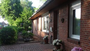 Un bâtiment en briques avec une cour dallée, des plantes en pot et un ciel dégagé.