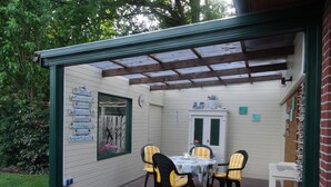 Une terrasse couverte avec une table et des chaises, un meuble en bois et un mur orné de panneaux.