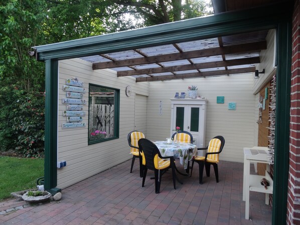 A covered patio with a table and chairs, a wooden cabinet, and a wall with signs.