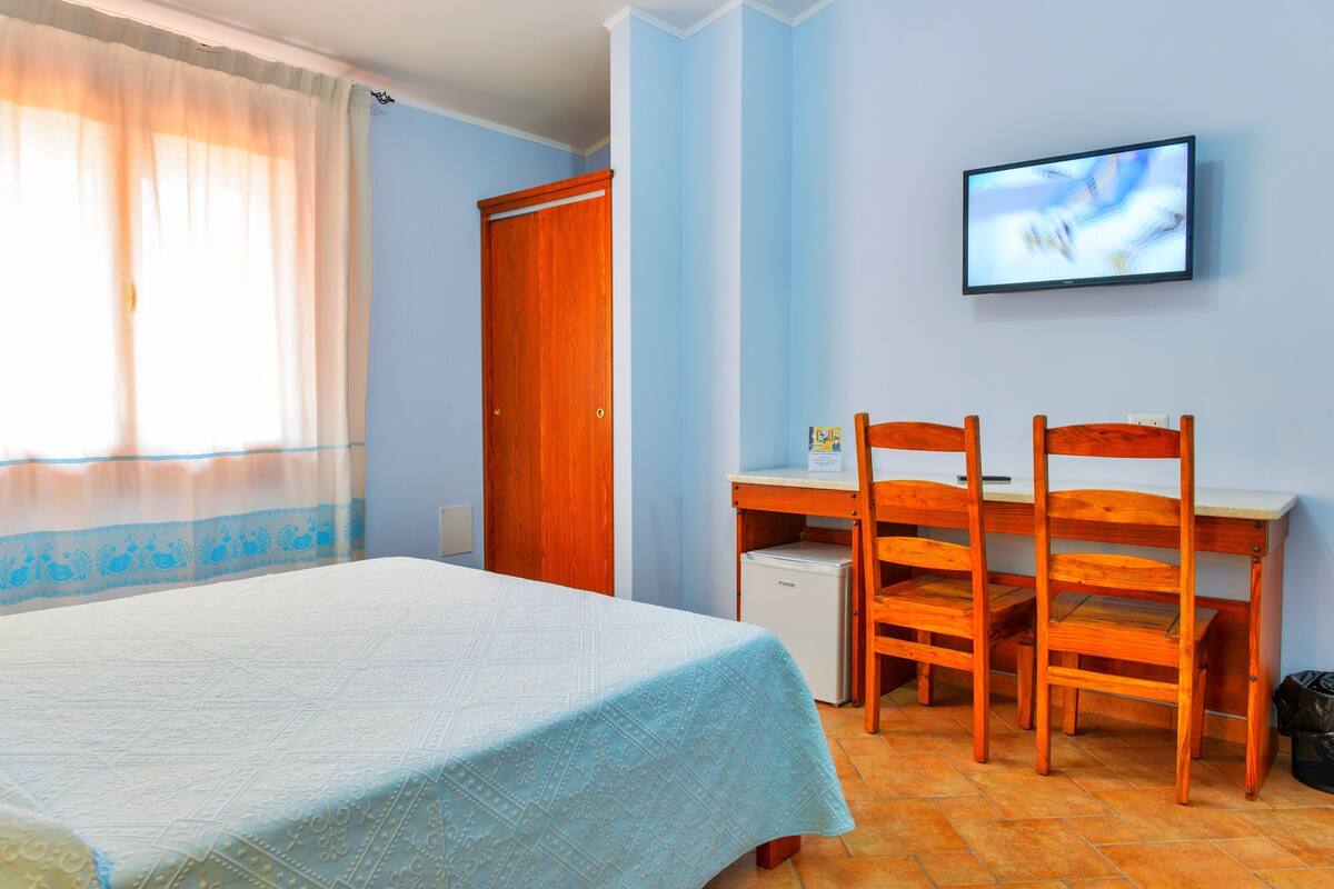 Un dormitorio con cama, escritorio, sillas, televisor y armario.