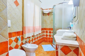 Un baño con inodoro, bidé, lavamanos y ducha.