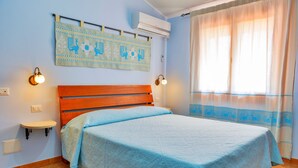 Un dormitorio con cama, aire acondicionado de pared, lámpara de pared y ventana con cortina.