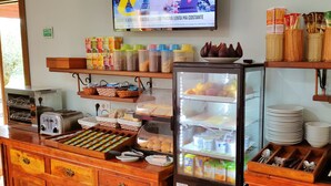 Un bufé de desayuno con diversas opciones de comida, un refrigerador y un televisor mostrando noticias.