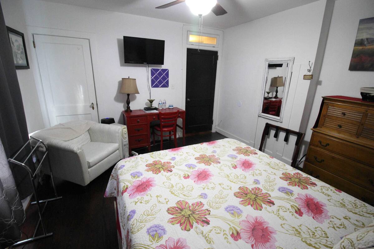 A bedroom with a bed, a desk, a chair, a dresser, a television, and a ceiling fan.