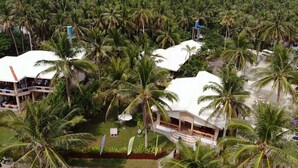Un resort con varias edificaciones de techo blanco rodeado de densas palmeras.