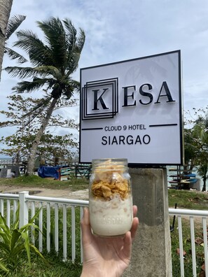 A hand holding a jar of cereal with milk in front of a hotel sign. - Kesa Cloud 9 Hotel & Resort Siargao (General Luna)