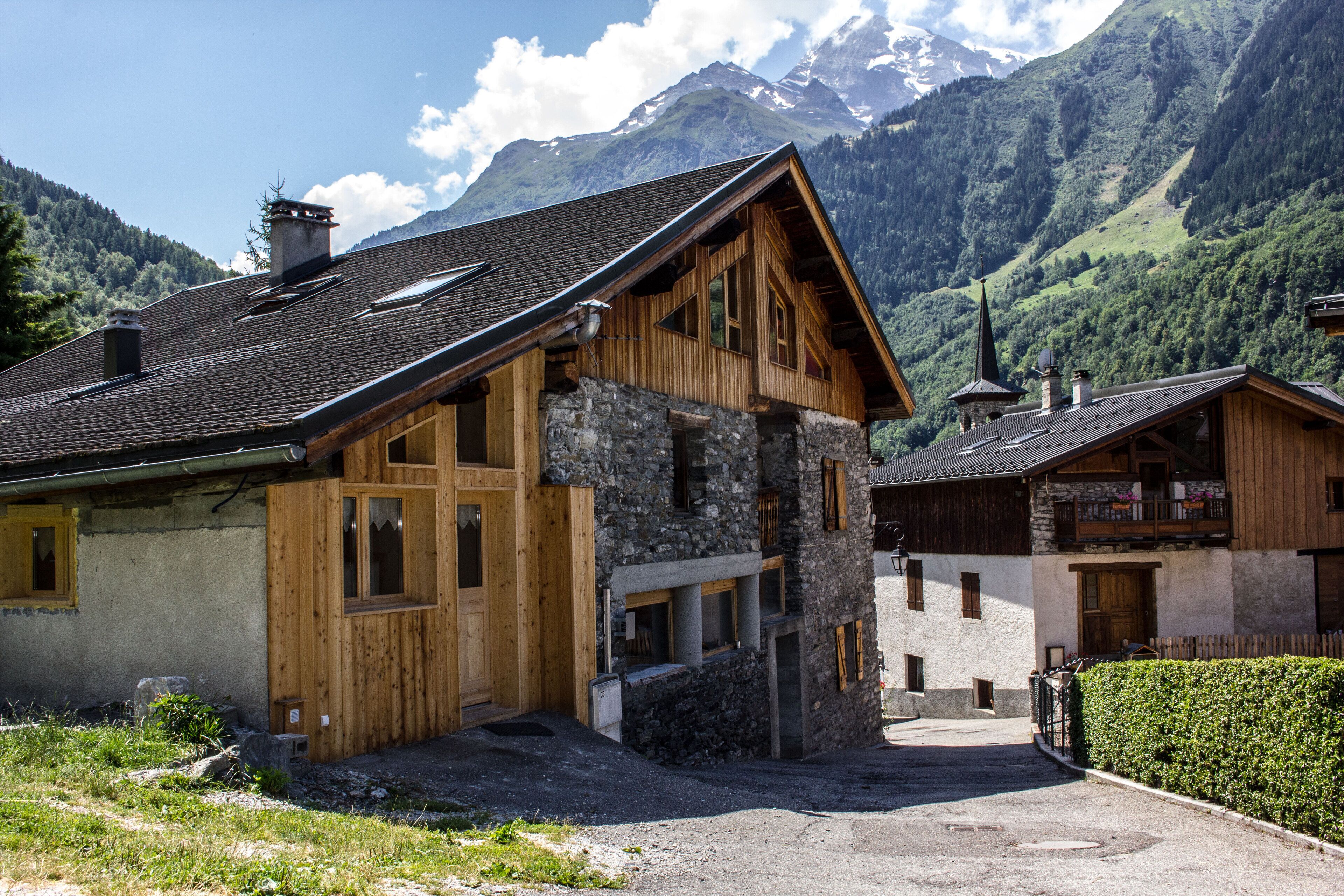 A traditional wooden chalet with a stone foundation, set against a backdrop of mountains.