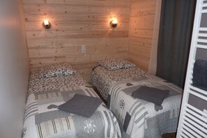 A room with two beds, each with patterned bedding and pillows. There are wall-mounted lights above the beds. - 3 star apartment, sleeps 9, in authentic Savoyard chalet (Sainte-Foy-Tarentaise)