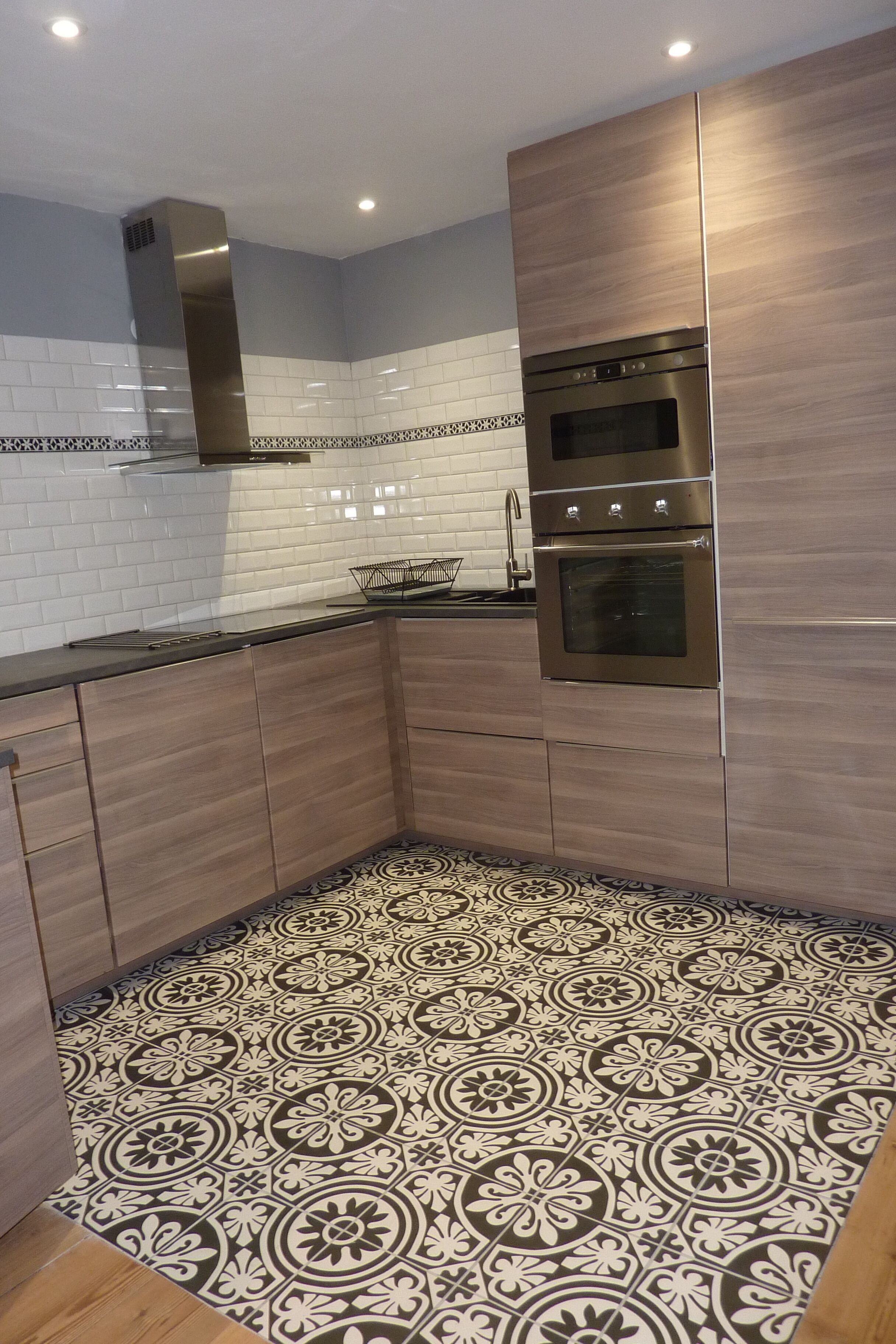 A modern kitchen with wooden cabinets, stainless steel appliances, and patterned floor tiles.