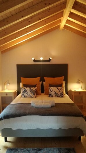 Une chambre avec un plafond en bois, un grand lit avec de nombreux oreillers, deux tables de chevet et un luminaire fixé au mur.