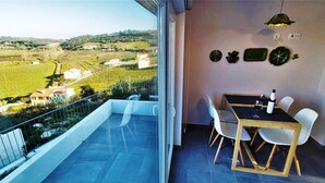 Un balcón con mesa y sillas, vistas a un viñedo y una pared decorada con platos.