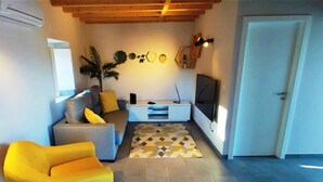 Una sala de estar con un sofá, un sillón amarillo, un televisor y un tapete estampado.