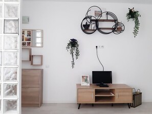 Une pièce moderne avec un bureau en bois, un écran noir et une étagère circulaire fixée au mur, ornée de plantes suspendues.