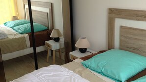 A hotel room with two beds, a bedside table with a lamp, a mirror, and a window with curtains. - Apartment with balcony and terrace near the center and the beach (Royan)