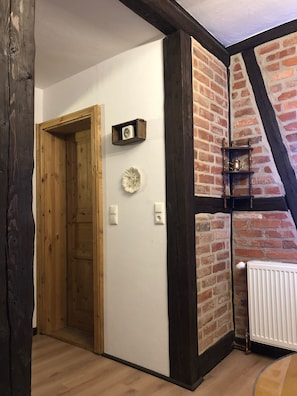 A hallway with a wooden door, a white wall, a brick wall, and a white radiator. - Apartment in the Harz Mountains (Wernigerode)