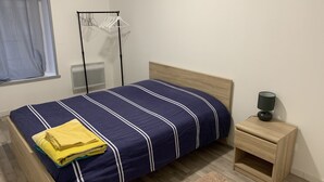 Een opgemaakt bed met een blauw-wit gestreept dekbed, een houten hoofdbord en een nachtkastje met een lamp.