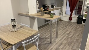 Een kleine keuken met een houten tafel en stoelen, een magnetron, een koffiezetapparaat en een wasmachine.