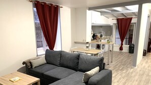 Een moderne woonkamer met een grijze hoekbank, een houten salontafel en een keuken op de achtergrond.