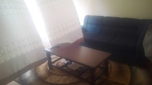 Een woonkamer met een donkerblauwe bank, een houten salontafel en een gordijn met een patroon.