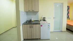 A compact kitchen with a sink, a small refrigerator, and a microwave. There is a door to the right and a colorful painting on the wall.
