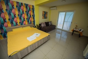 Quarto com cama grande, sofá, painel de parede colorido e porta de vidro deslizante.